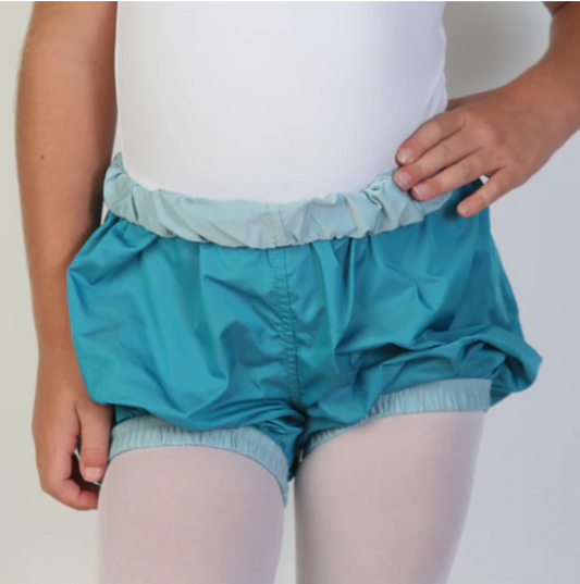 A young ballerina wears dark teal trash-bag style shorts with a light blue waistband.